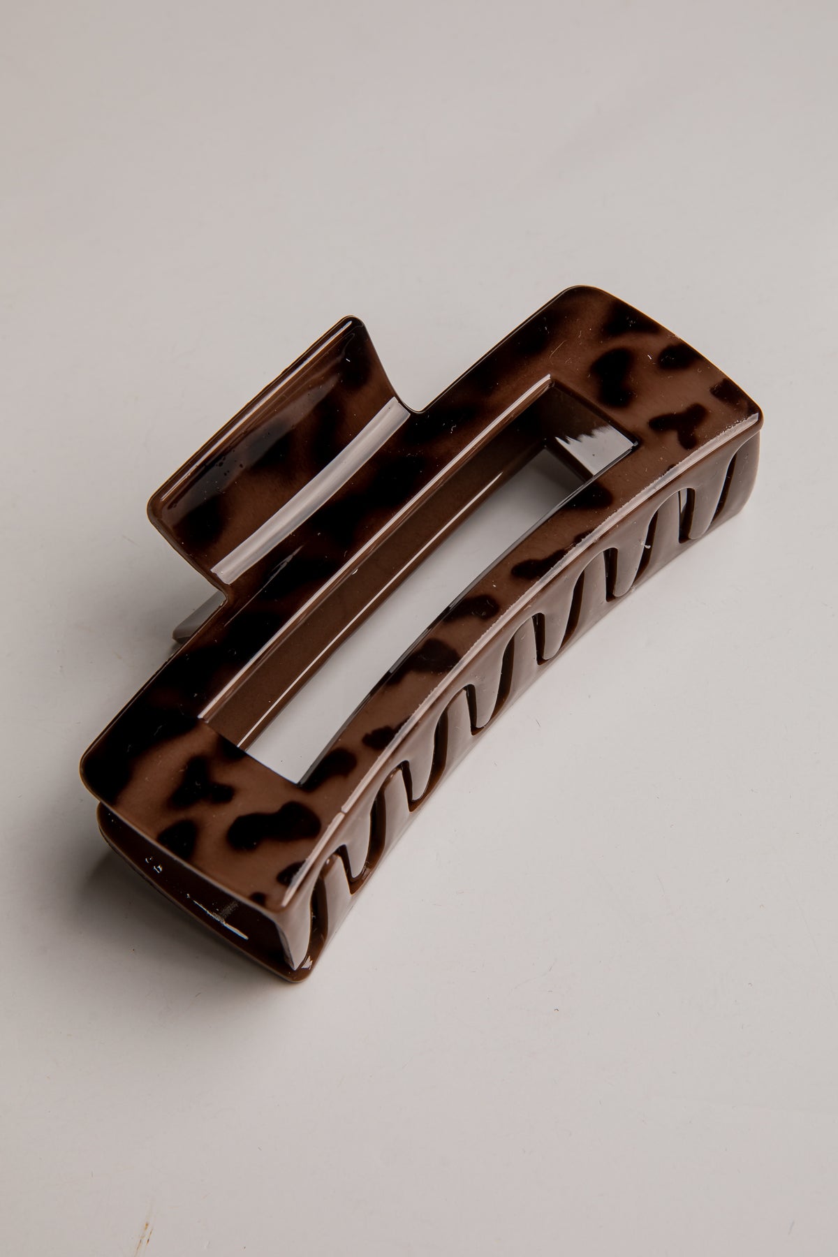 A rectangular hair claw clip with a glossy brown and black tortoiseshell pattern, photographed on a neutral light gray background.