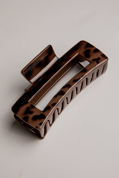 A rectangular hair claw clip with a glossy brown and black tortoiseshell pattern, photographed on a neutral light gray background.