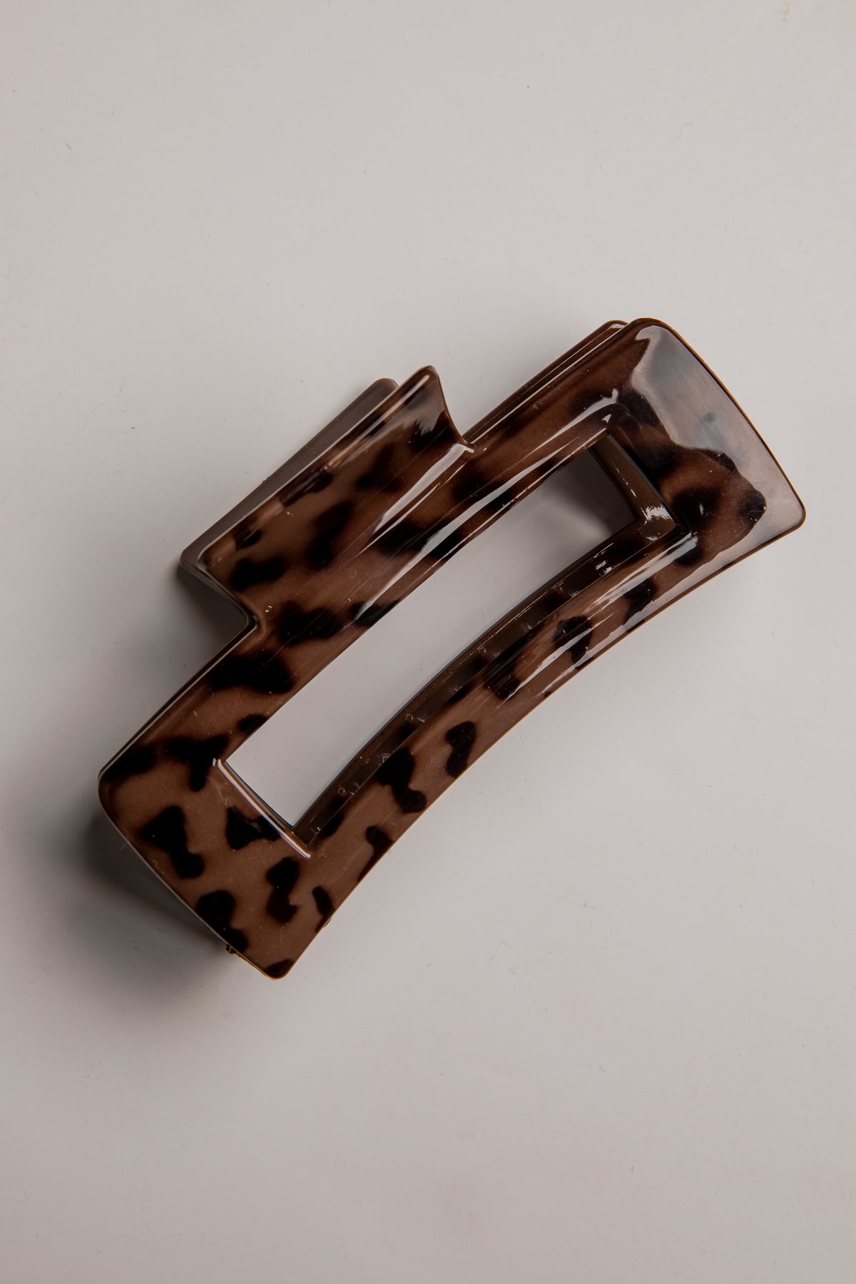 A glossy tortoiseshell hair claw clip in brown and black, photographed on a neutral light gray background.