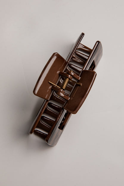 A glossy dark brown hair claw clip shown from an overhead angle on a light gray background.