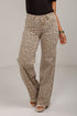 A person wearing leopard-print pants with a black top and beige platform sandals, standing against a light gray studio background.