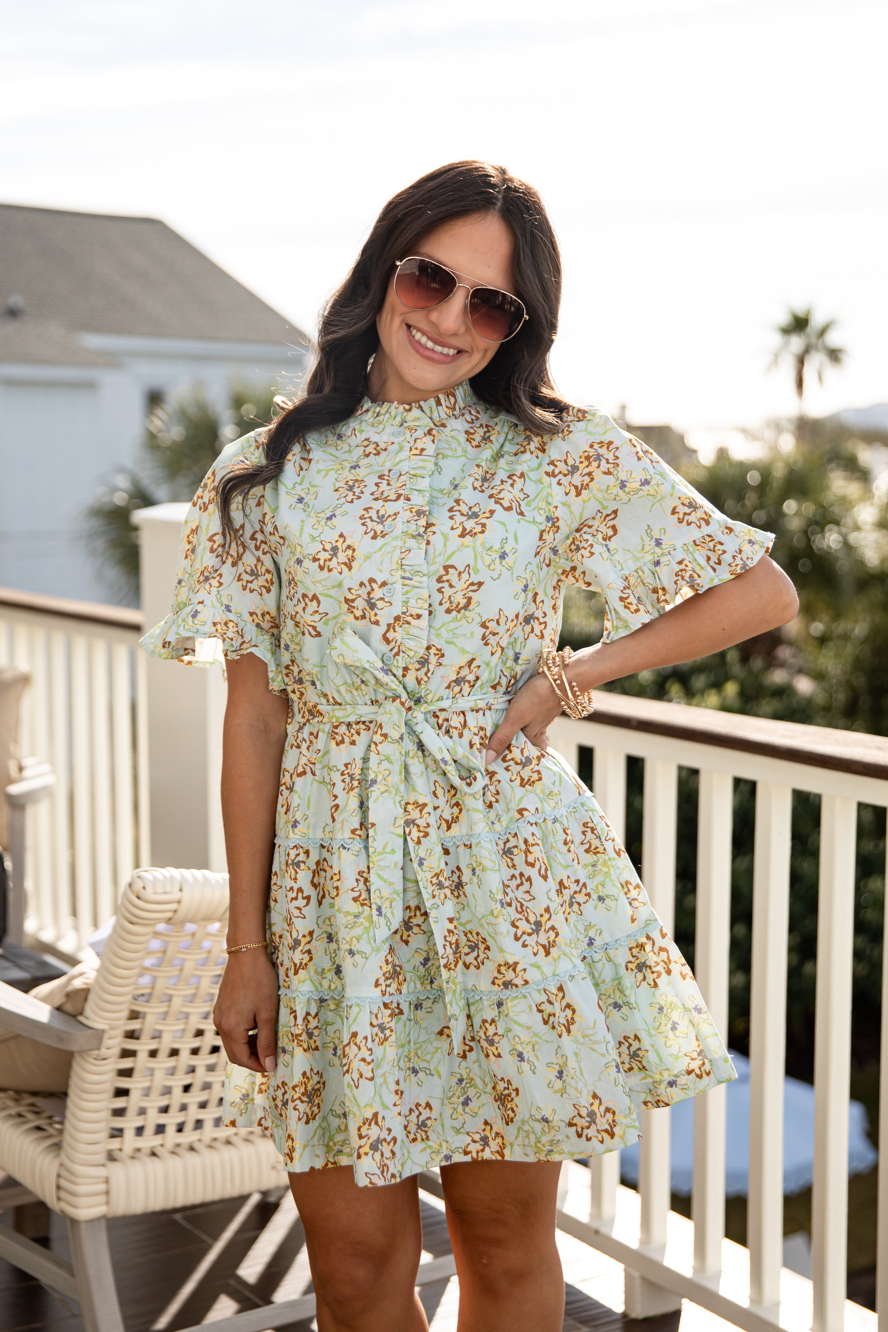 Woman wearing a spring floral mini dress with sunglasses and gold bracelets