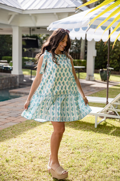 Woman in a light blue dress with a pineapple pattern standing in a garden.
