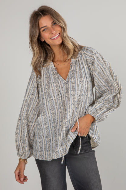 Woman wearing a patterned blouse and dark jeans against a plain background