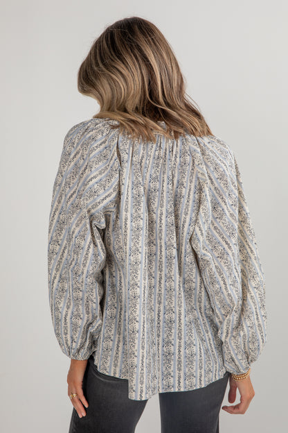 Woman wearing a patterned blouse with long sleeves on a plain background