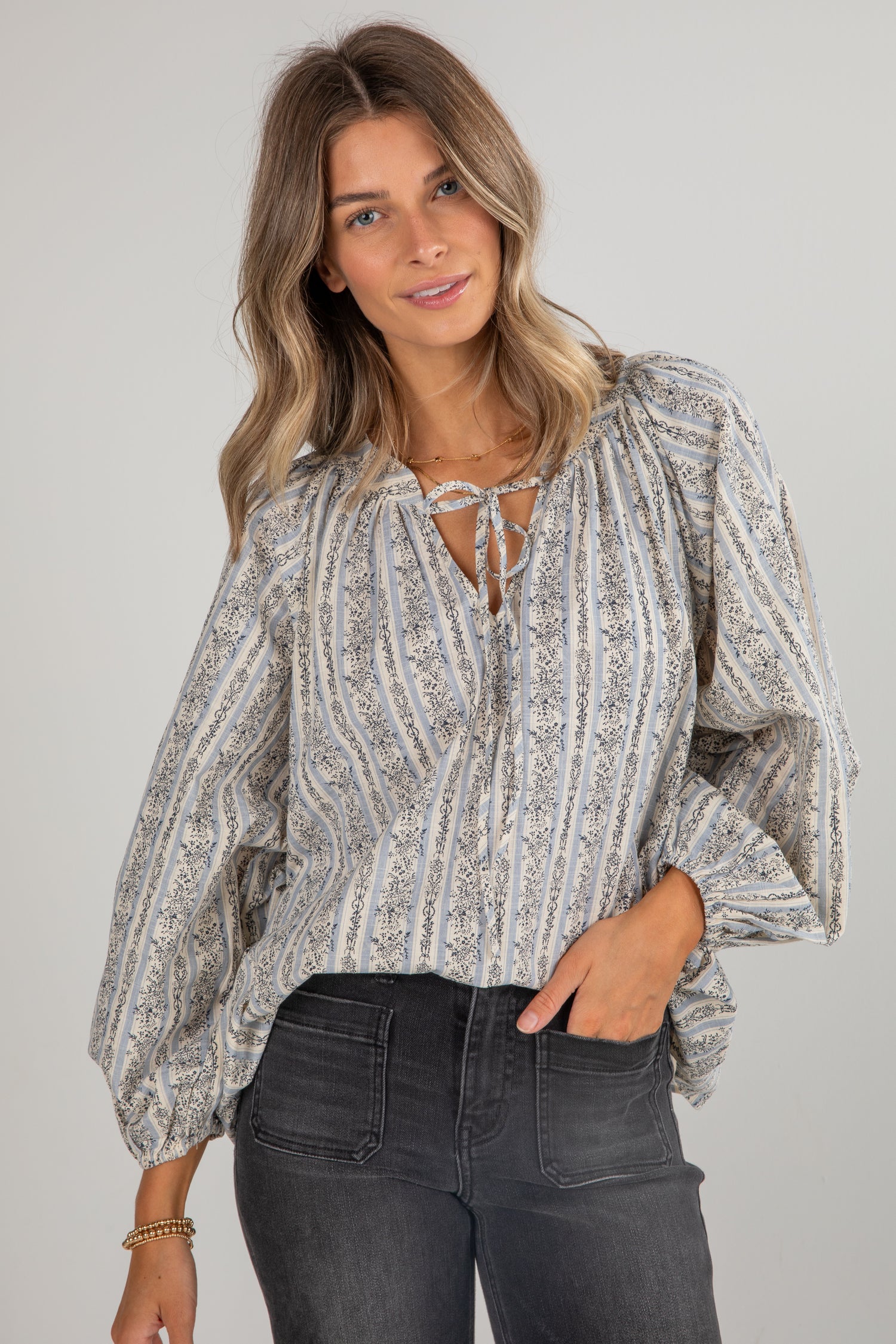Woman wearing a patterned blouse and black pants against a plain background
