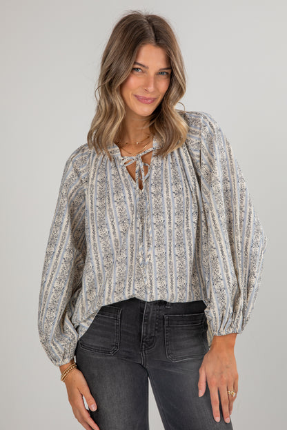 Woman wearing a patterned blouse and dark jeans against a plain background