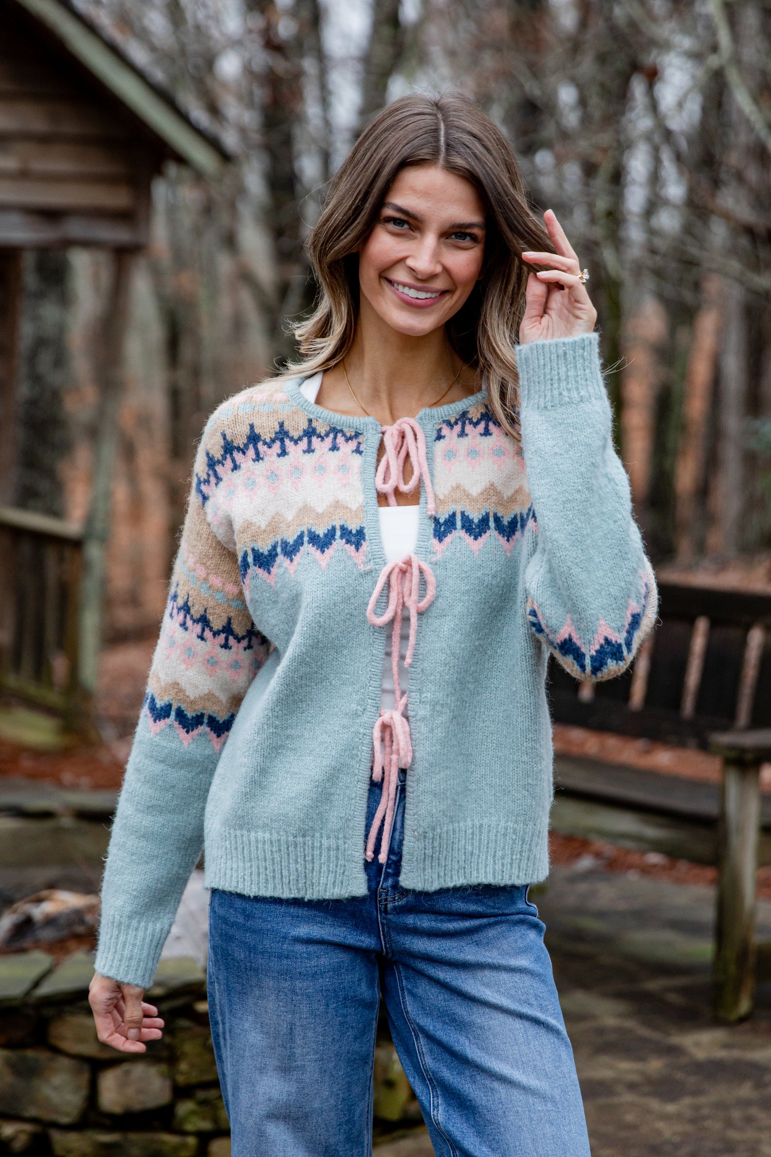 Woman wearing a patterned cardigan outdoors with a wooden cabin in the background