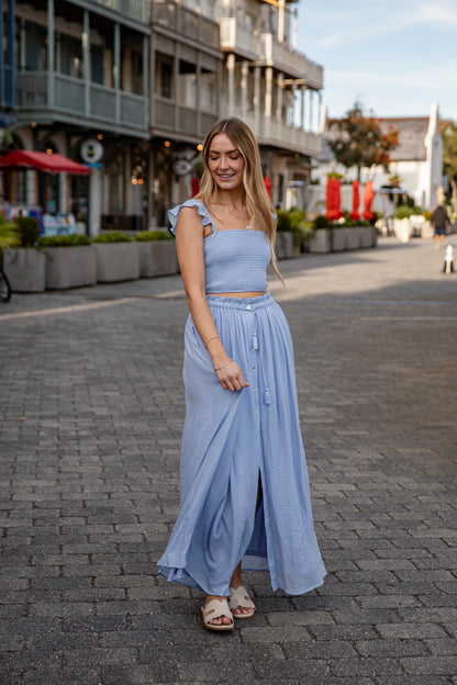 Woman in a light blue outfit standing on a street with shops in the background