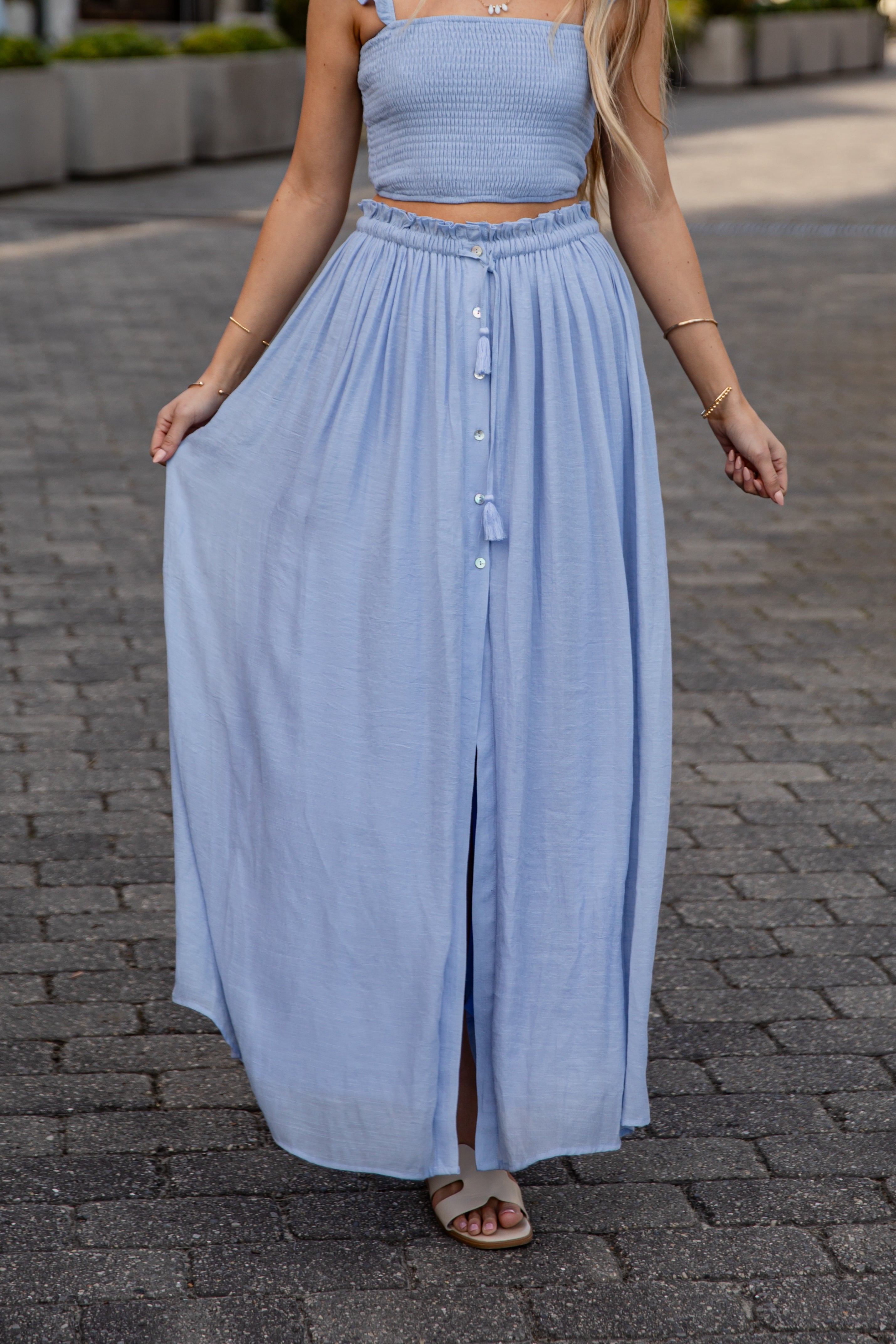 Woman wearing a light blue dress with a button front and wide leg on a paved street.