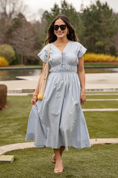 Woman in a light blue dress walking outdoors with a scenic background