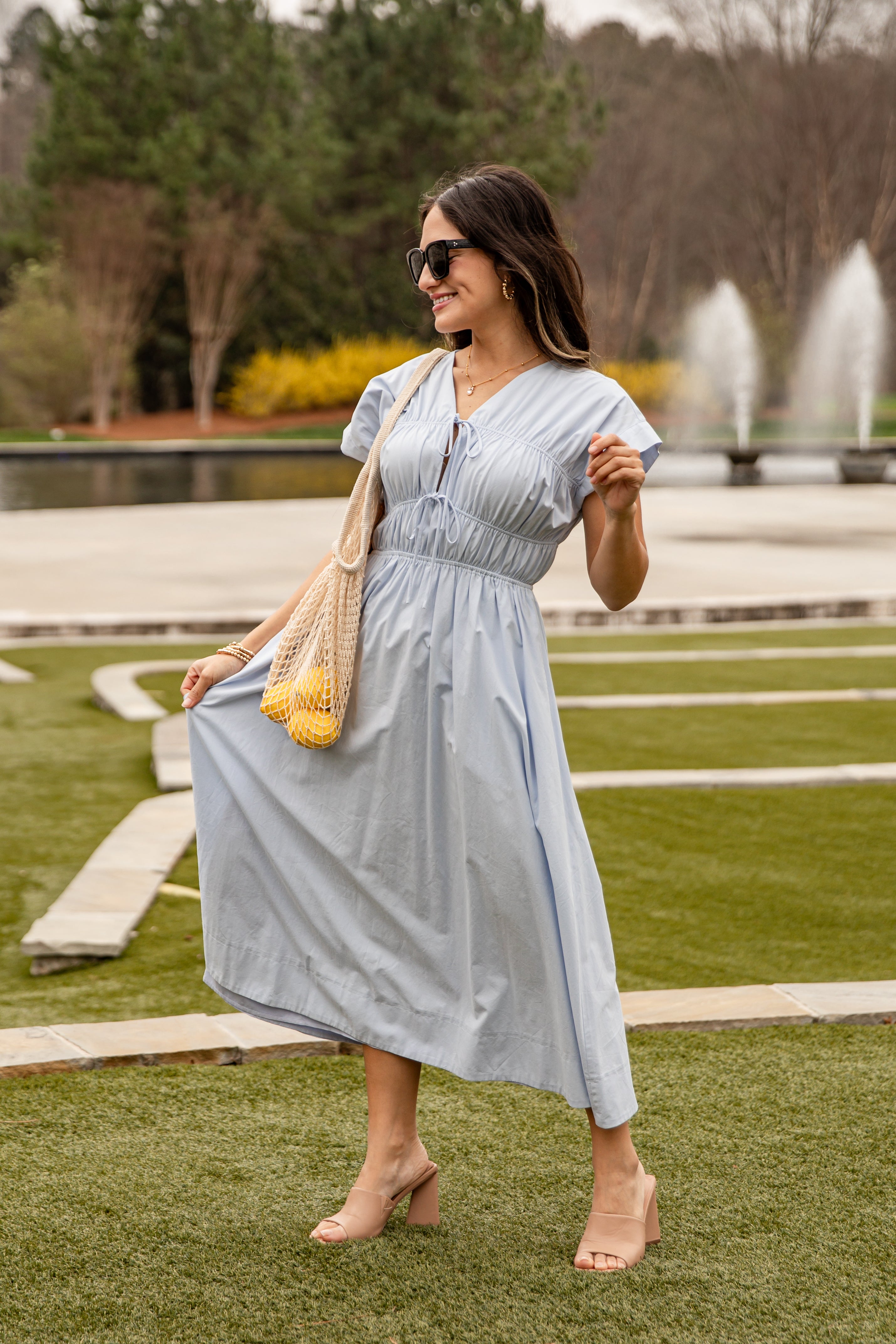 Woman in a light blue dress standing outdoors with a fountain in the background