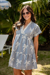 Woman wearing a blue dress with palm tree patterns outdoors.