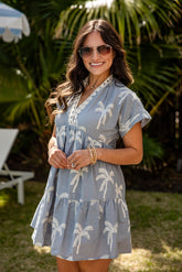 Woman wearing a blue dress with palm tree pattern outdoors