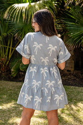 Woman wearing a light blue dress with palm tree patterns in an outdoor setting.