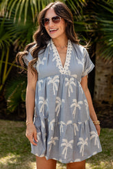 Woman wearing a light blue dress with palm tree patterns outdoors.