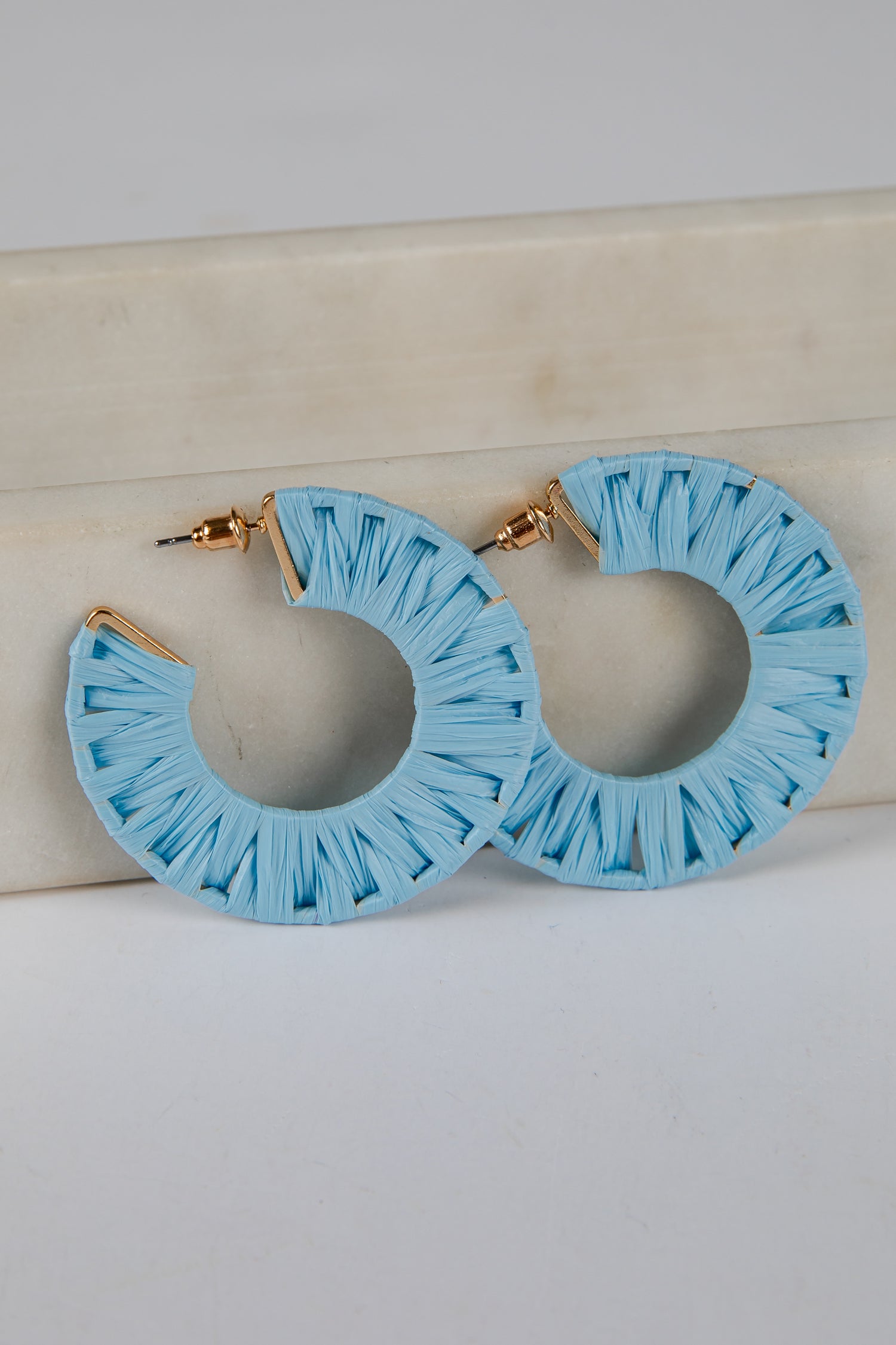 Light blue hoop earrings with ruffled edges on a light gray background