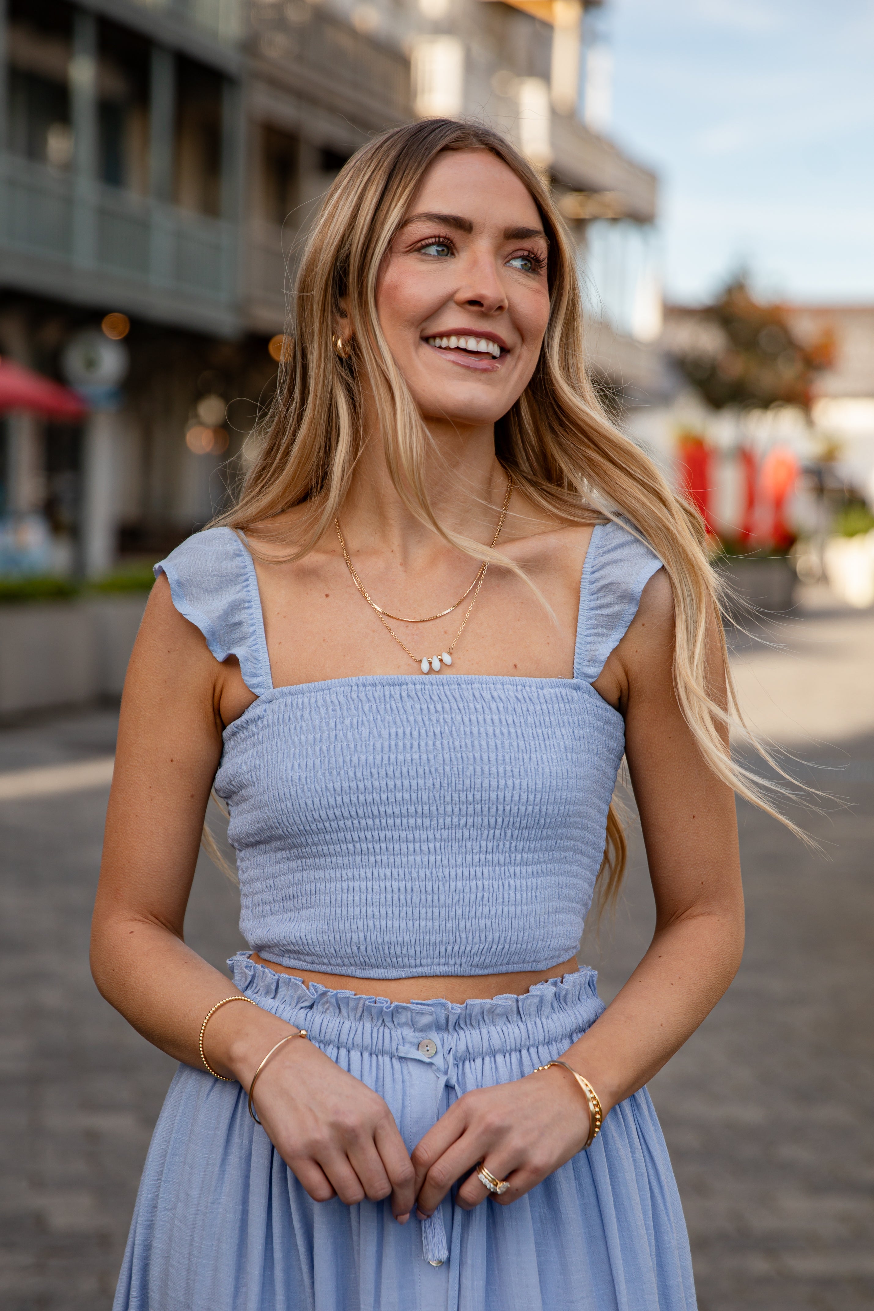 Woman wearing a light blue top and skirt standing on a street.