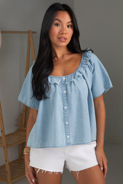 Woman wearing a light blue denim top and white shorts in a neutral setting