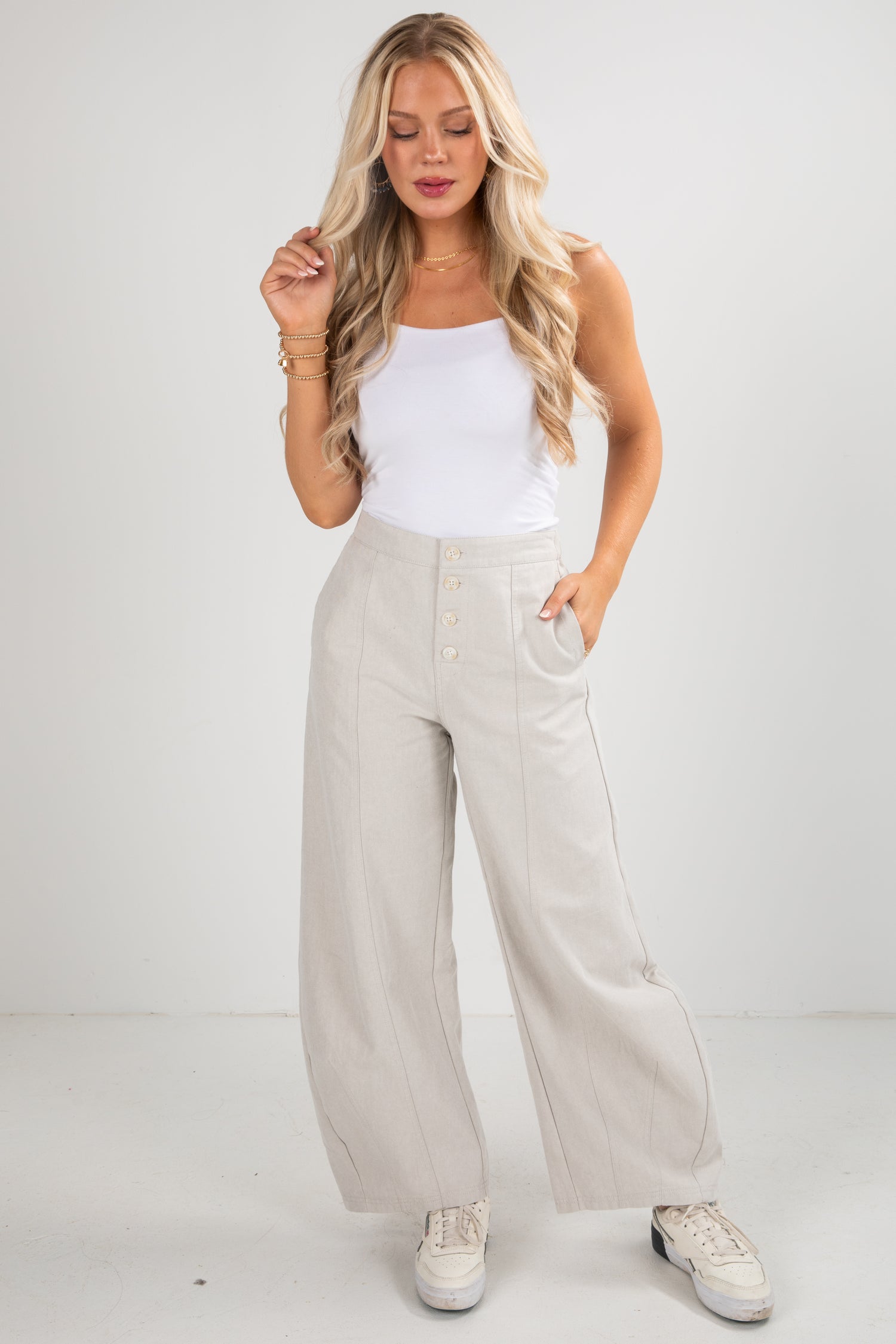 Woman wearing a white tank top and beige wide-leg pants against a plain background