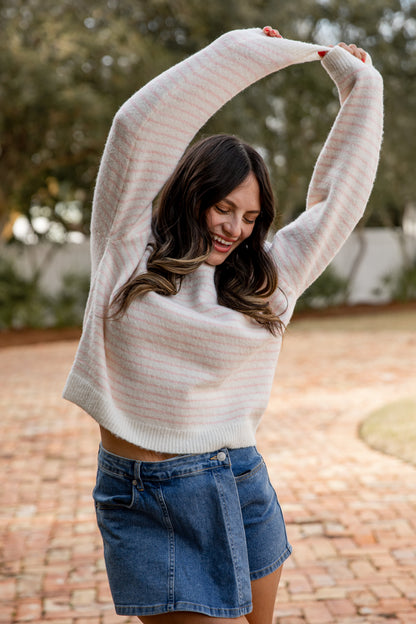 Woman wearing a light gray sweater and denim shorts outdoors