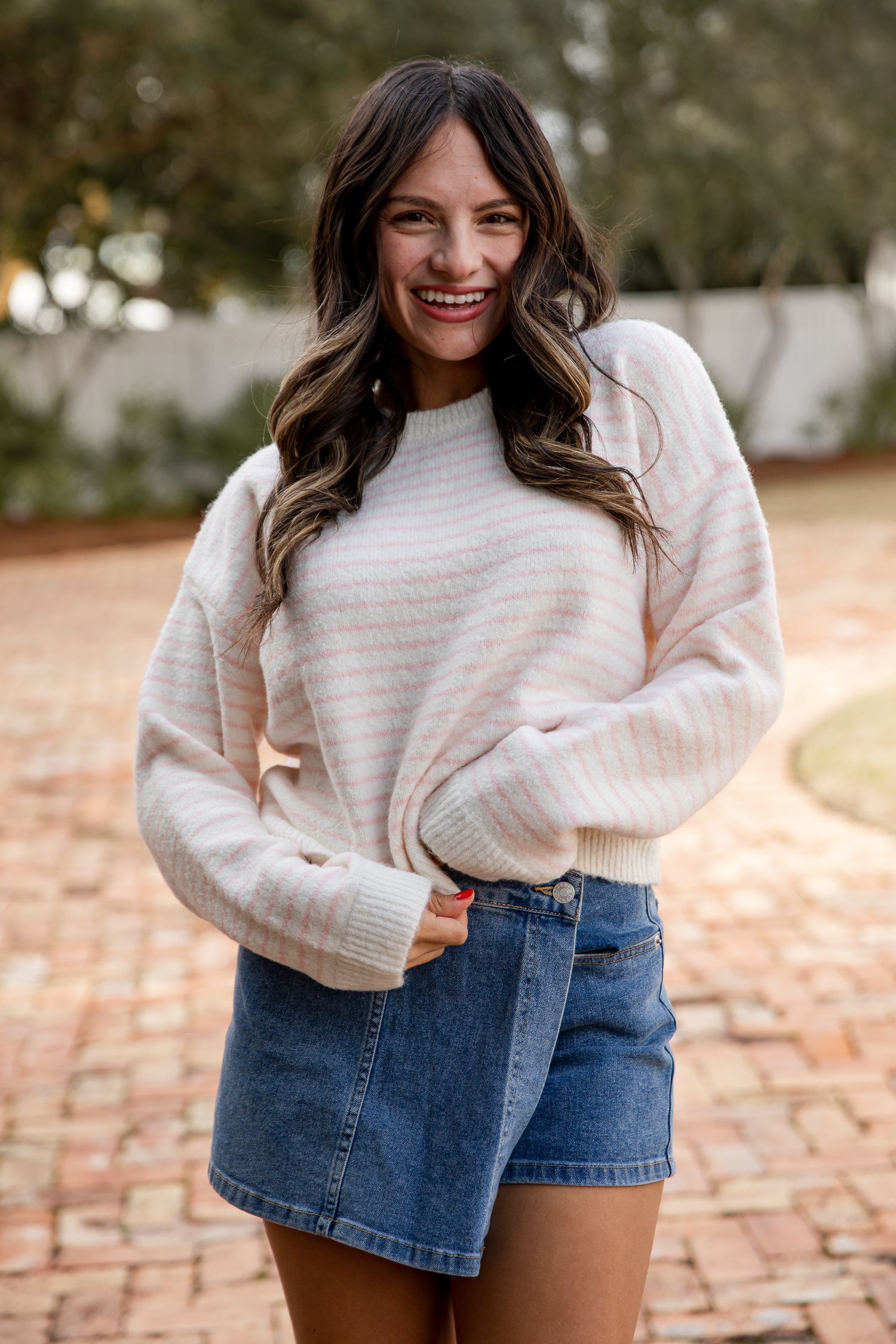 Woman wearing a cream sweater and denim skirt outdoors