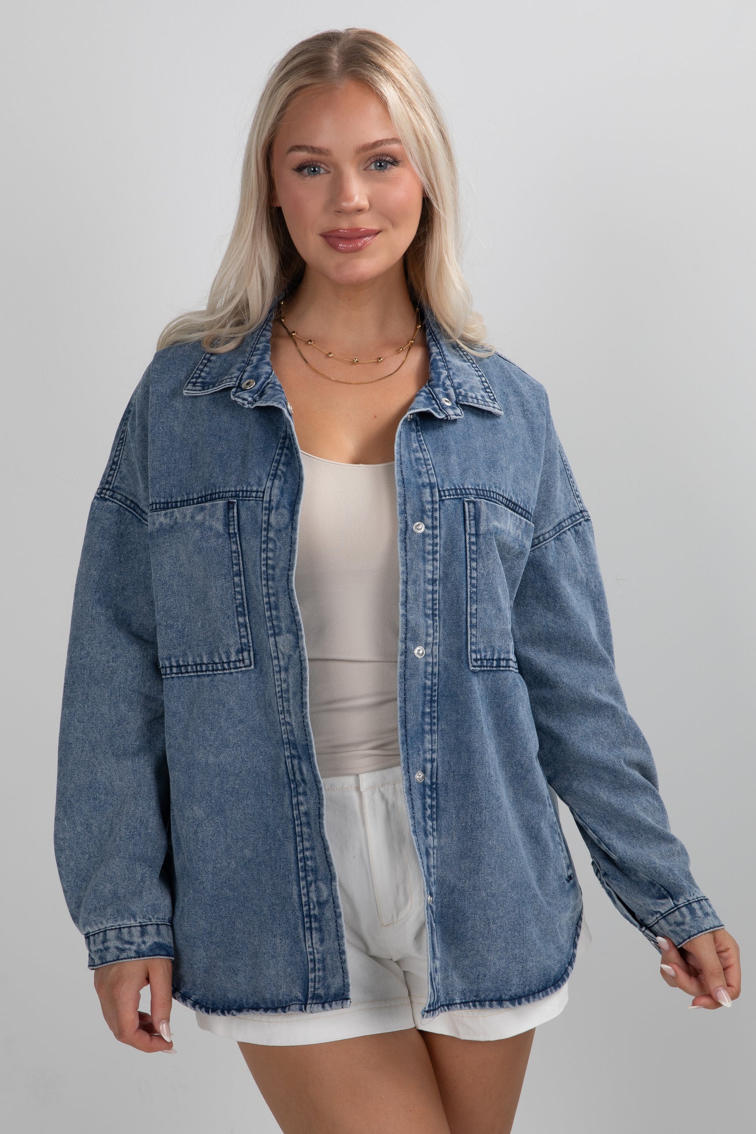 Woman wearing a blue denim jacket over a white top and shorts on a gray background