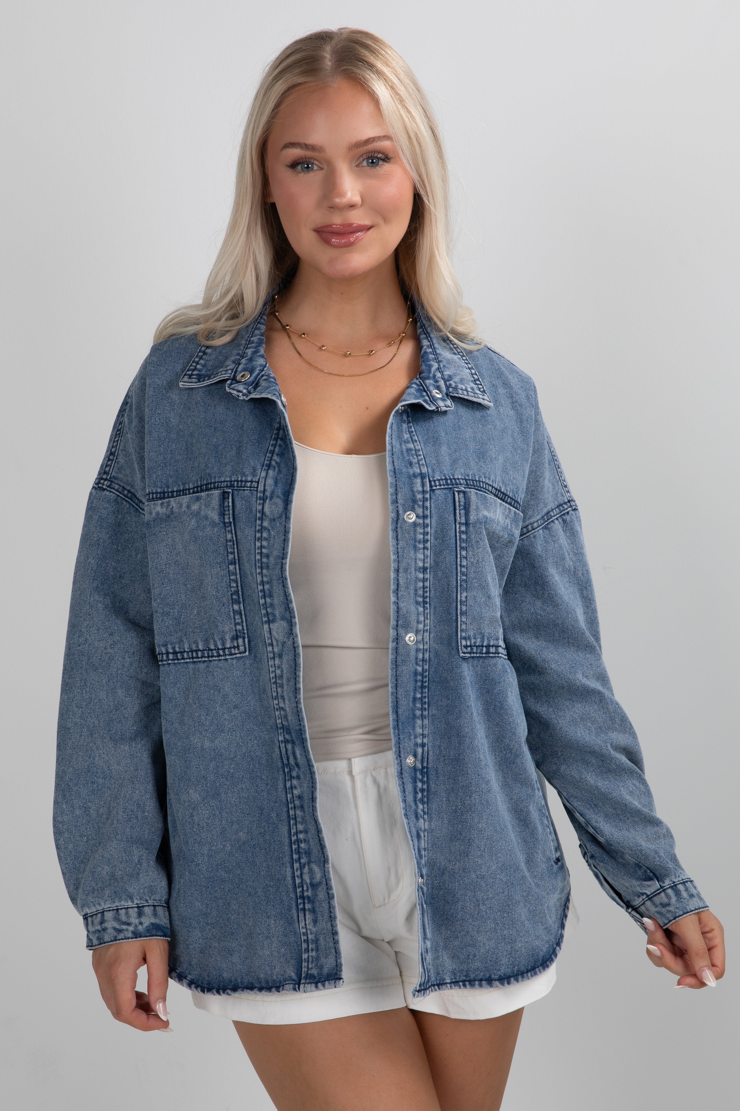 Woman wearing a blue denim jacket over a white top and shorts on a gray background
