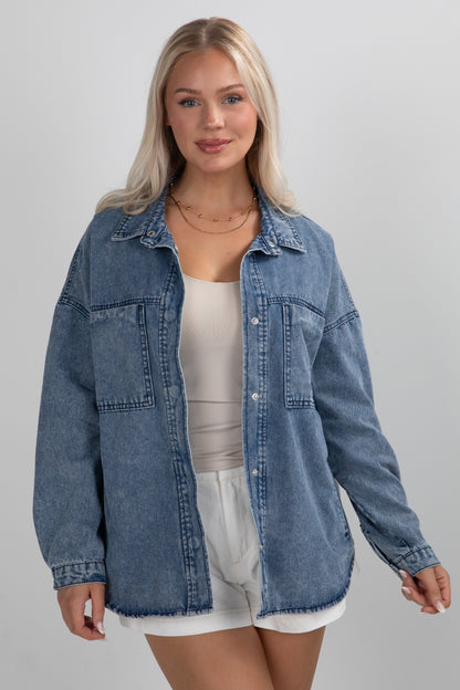 Woman wearing a blue denim jacket over a white top and shorts on a gray background