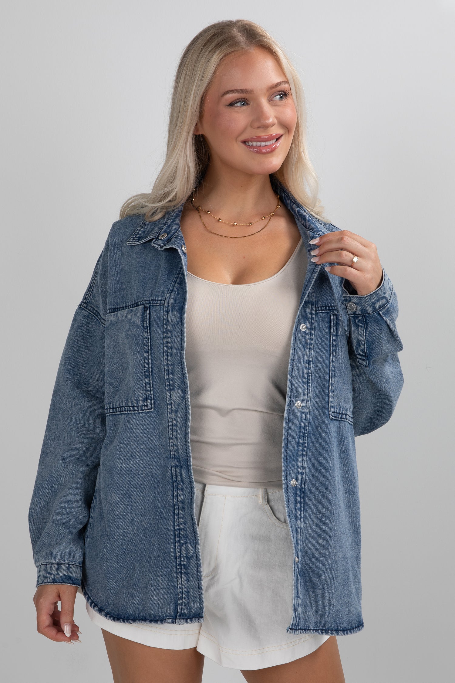 Woman wearing a denim jacket over a white top and shorts on a gray background