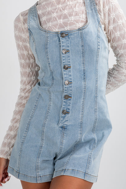 Denim overall shorts with a white lace top on a plain background