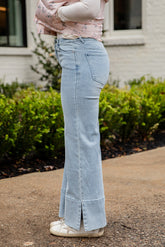 Person wearing light blue flared jeans standing outdoors on a sidewalk.
