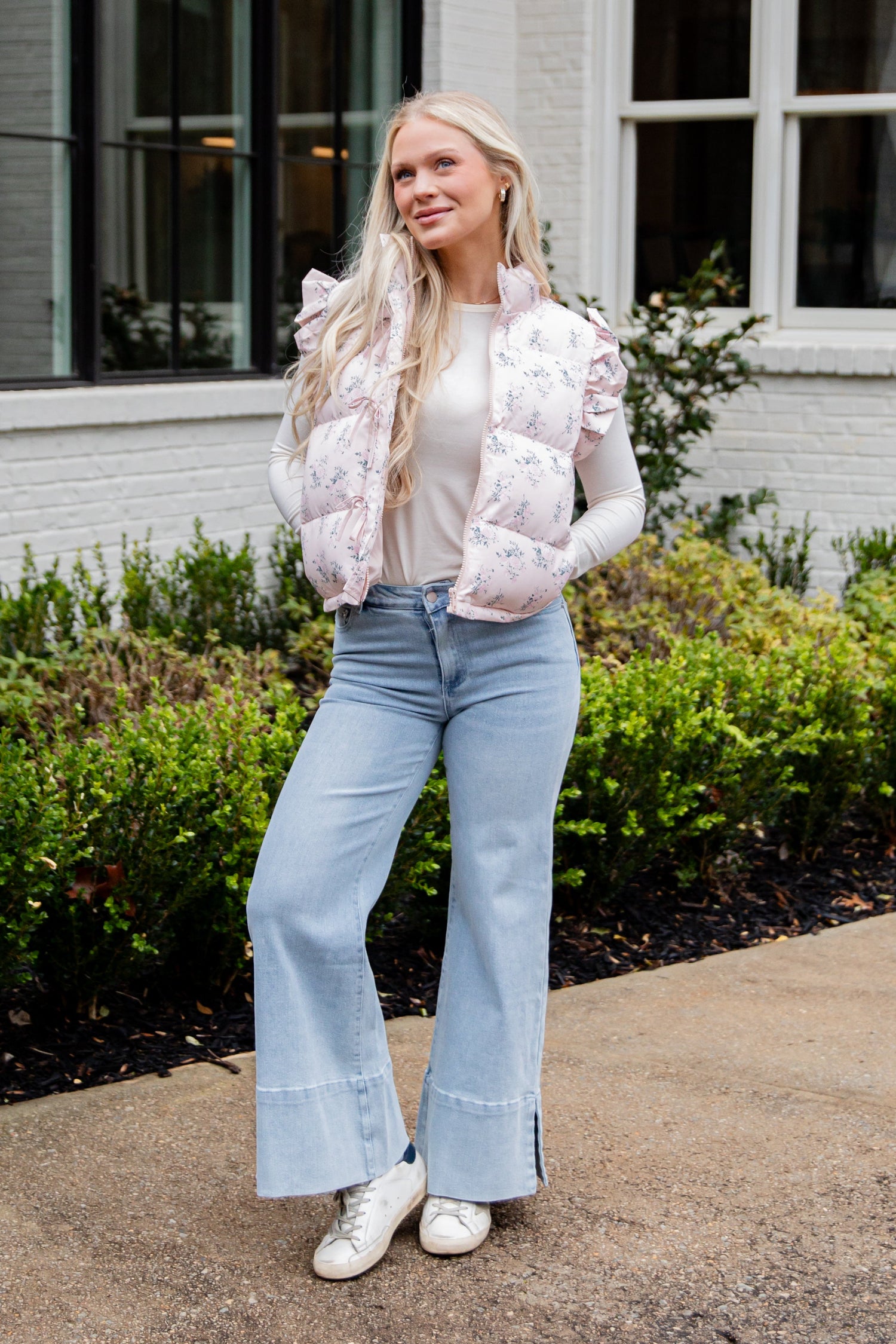 Woman wearing a white puffer vest and light blue jeans standing outdoors.