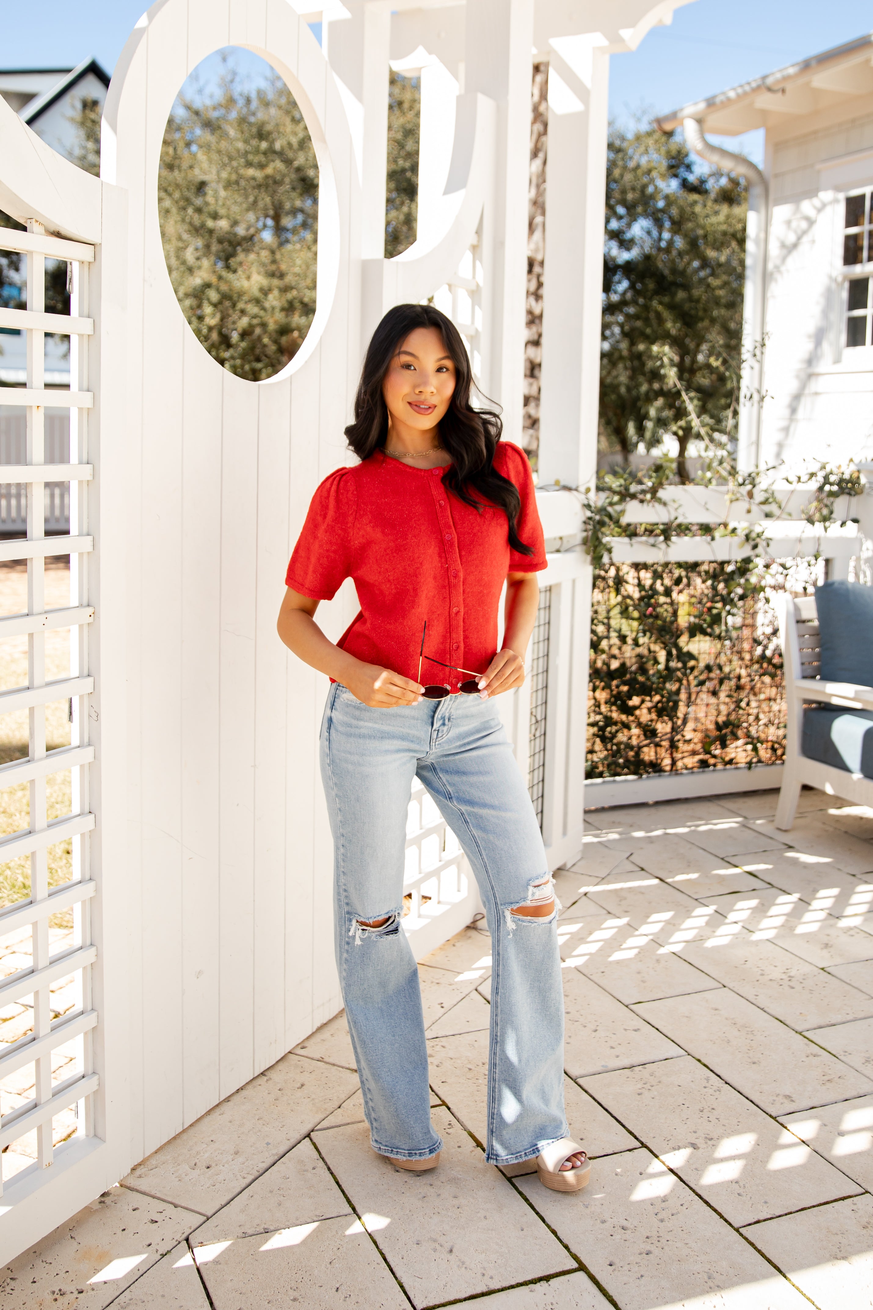 Woman in a red blouse and light blue jeans standing on a patio