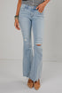 A person wearing light-wash blue distressed flare jeans with frayed hems, paired with tan pointed-toe heels and a gray top, standing against a plain light gray studio background.