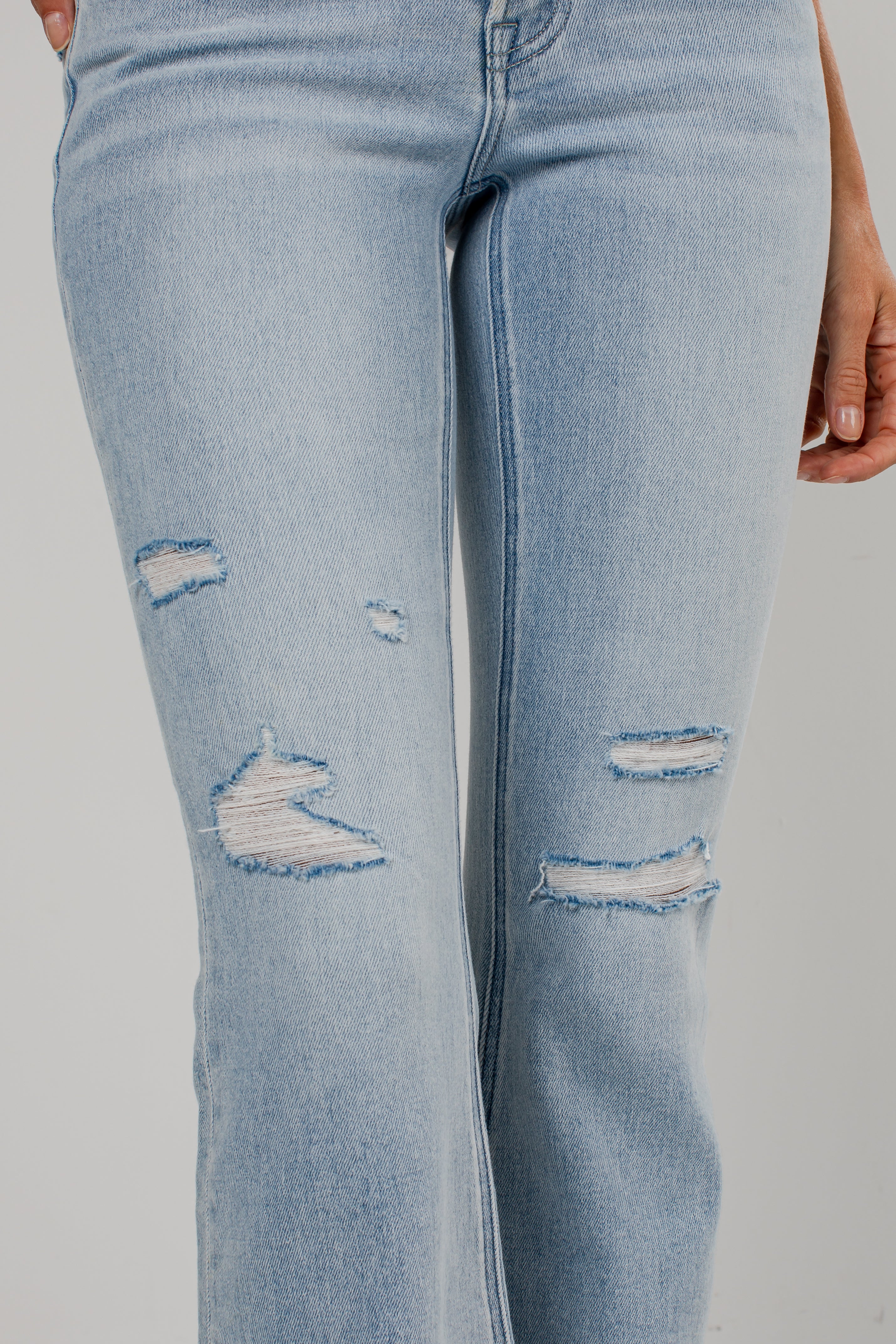 Light wash blue distressed jeans with ripped details on the thighs, shown on a model against a light gray background.