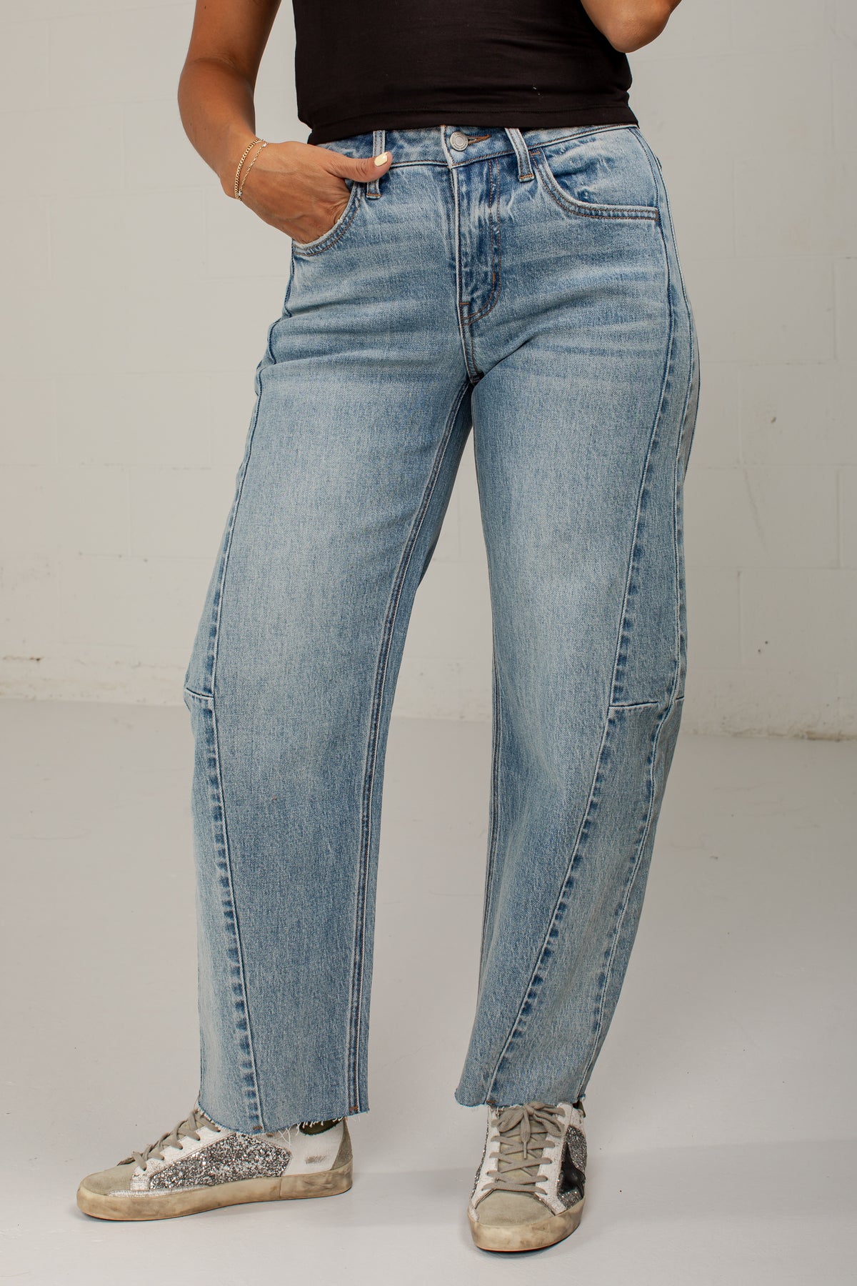 A person wearing light-wash blue wide-leg jeans with side cargo pockets, paired with a black top and distressed sneakers, standing against a plain light gray wall.