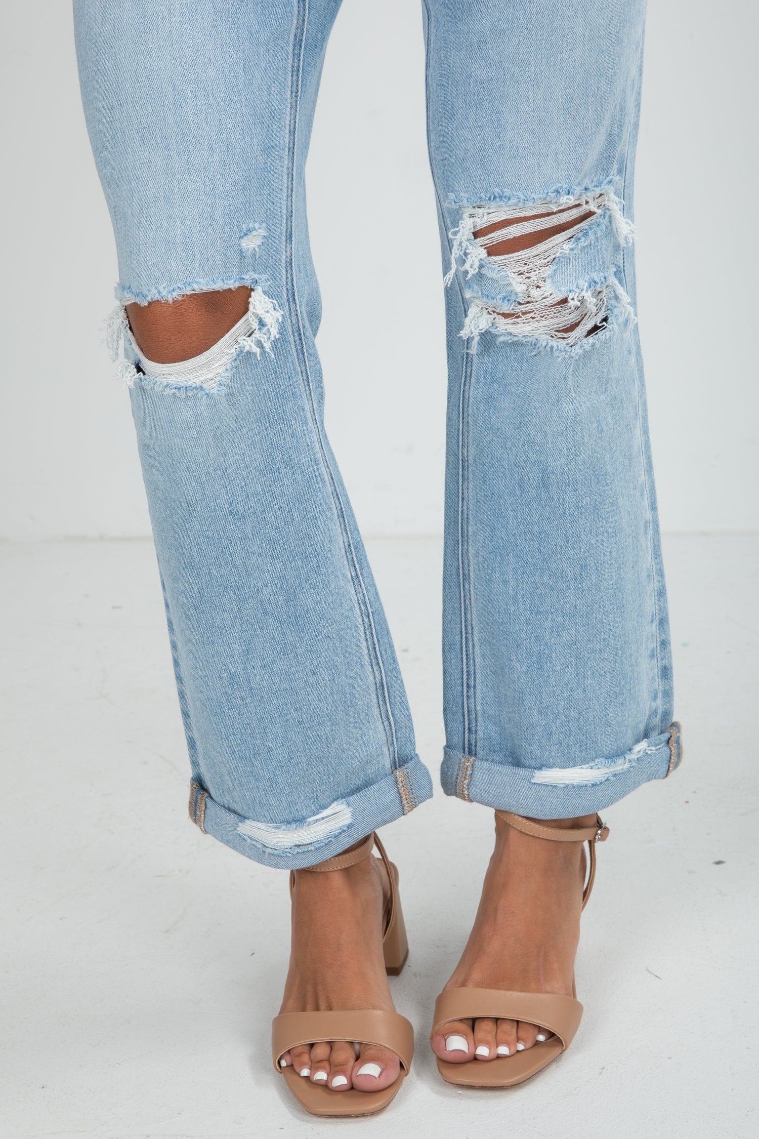 Light blue distressed jeans worn with brown open-toe sandals on a white background