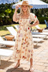Woman in a floral dress and sun hat standing in a sunlit outdoor setting with lounge chairs and umbrellas.