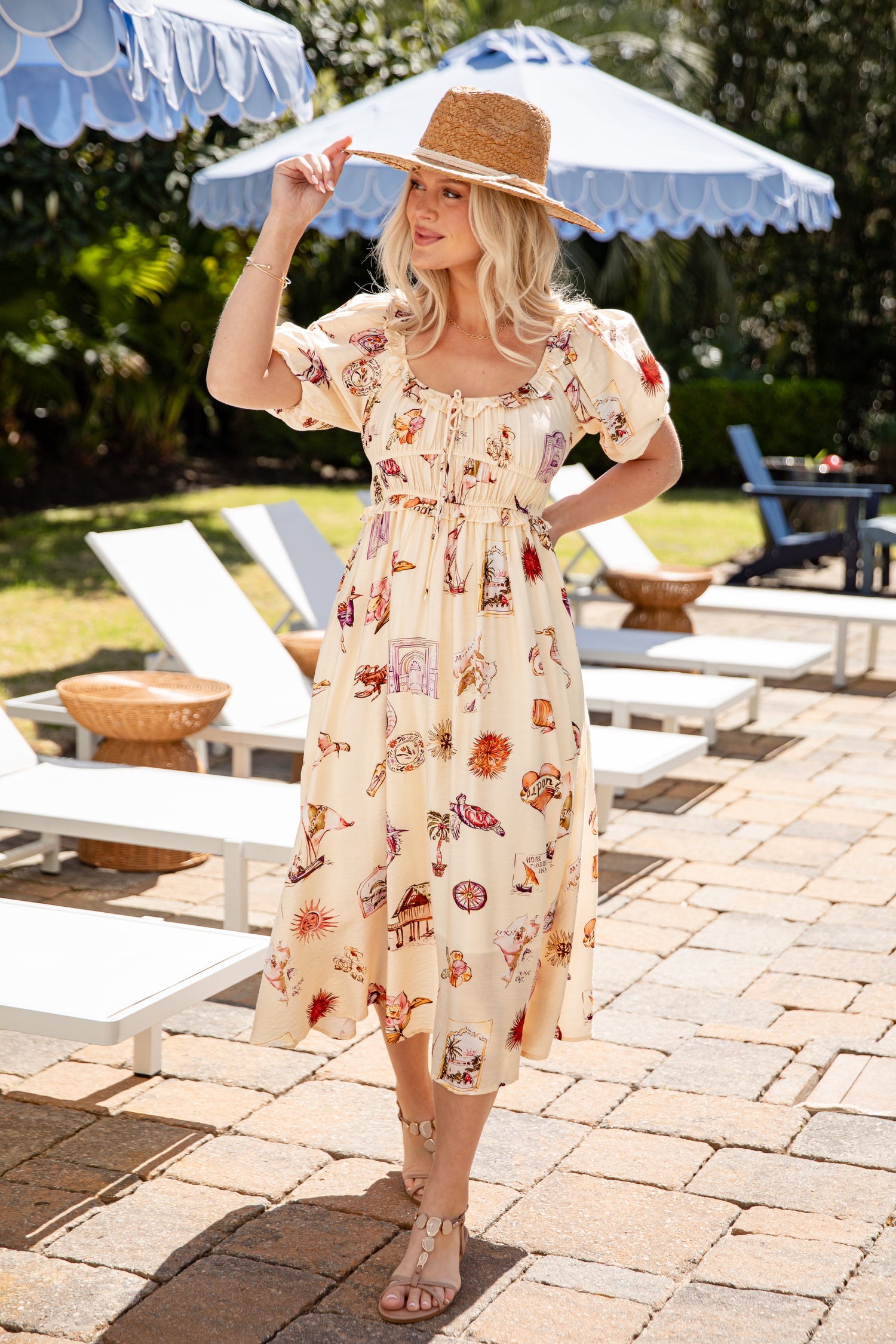 Woman in a floral dress standing outdoors with lounge chairs and umbrellas in the background