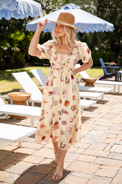 Woman in a floral dress standing outdoors with lounge chairs and umbrellas in the background