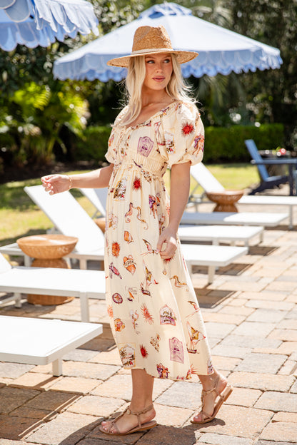 Woman in a floral dress and hat standing in a sunlit outdoor setting with lounge chairs and umbrellas.
