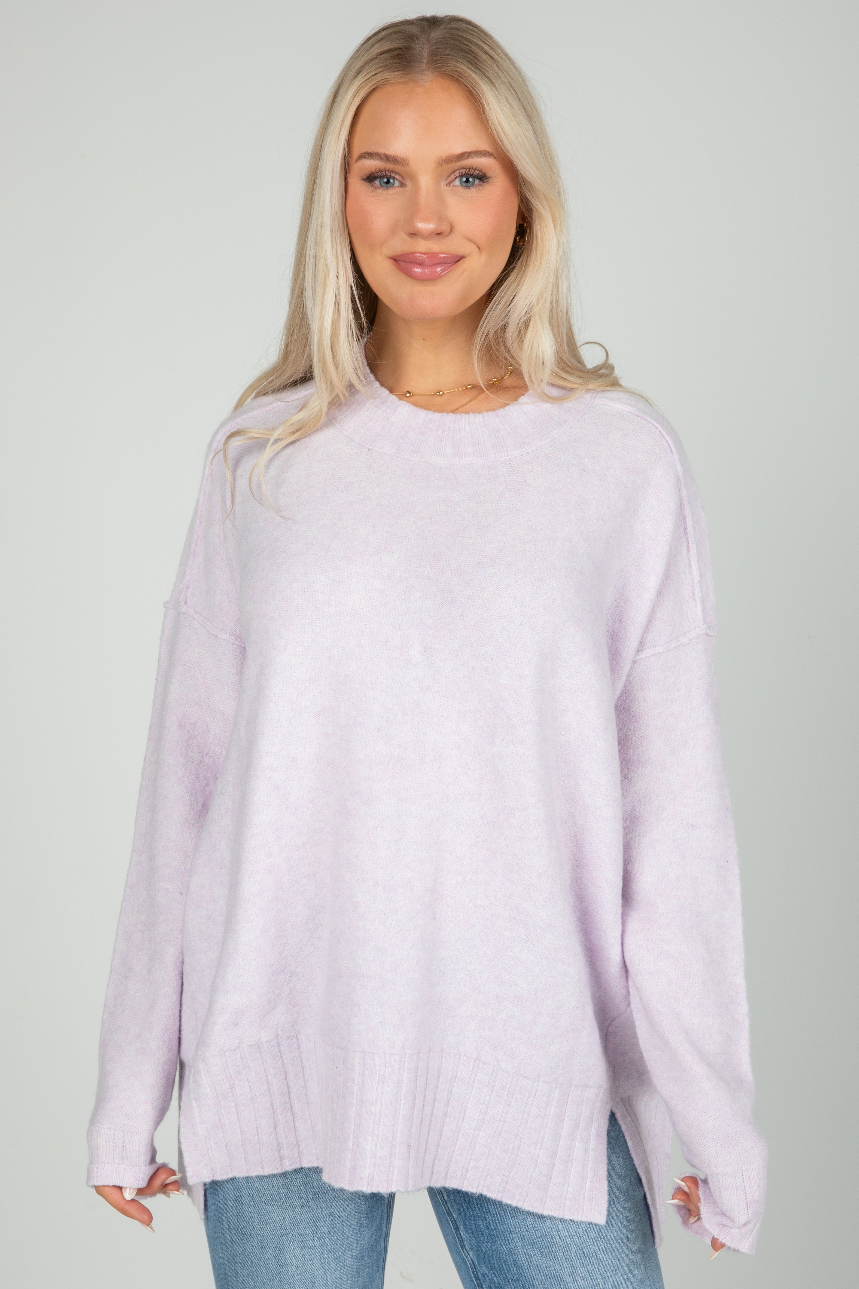 Woman wearing a light purple sweater and blue jeans against a plain background