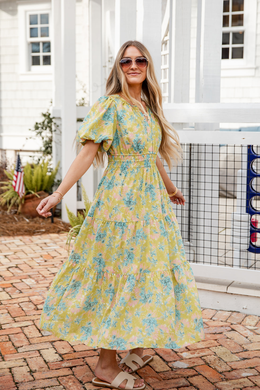 Woman wearing a yellow floral dress standing on a brick patio.