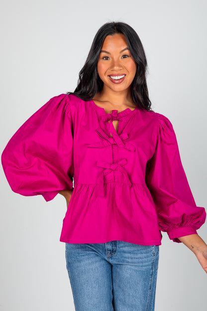 Woman wearing a bright pink blouse with puffed sleeves on a plain background