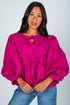 Woman wearing a bright pink blouse with puffed sleeves against a plain background
