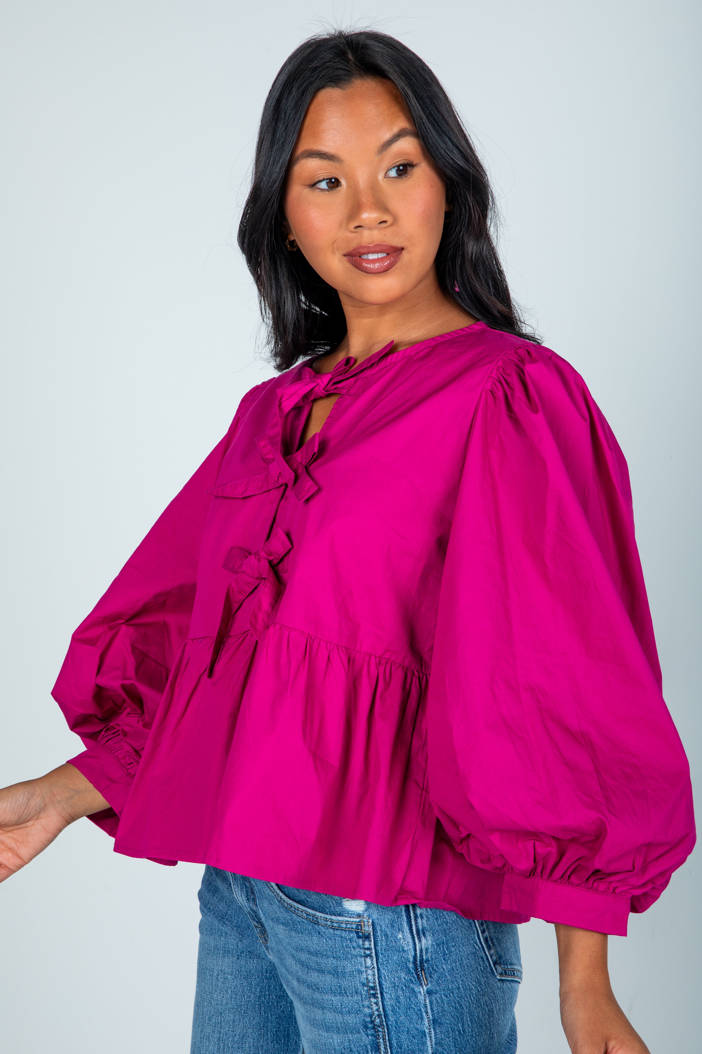 Woman wearing a bright pink blouse with balloon sleeves against a plain background