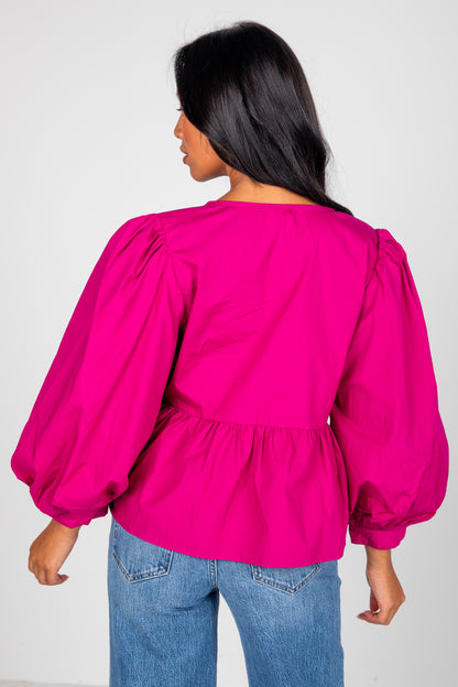 Person wearing a bright pink blouse with puffed sleeves and blue jeans on a white background