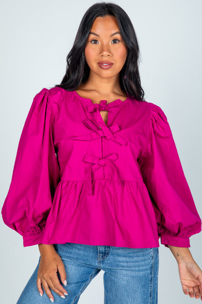 Woman wearing a bright pink blouse with puffed sleeves and blue jeans on a plain background