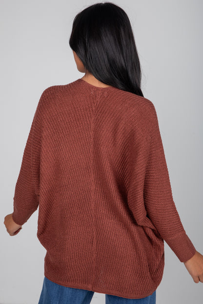 Person wearing a brown textured sweater on a plain background